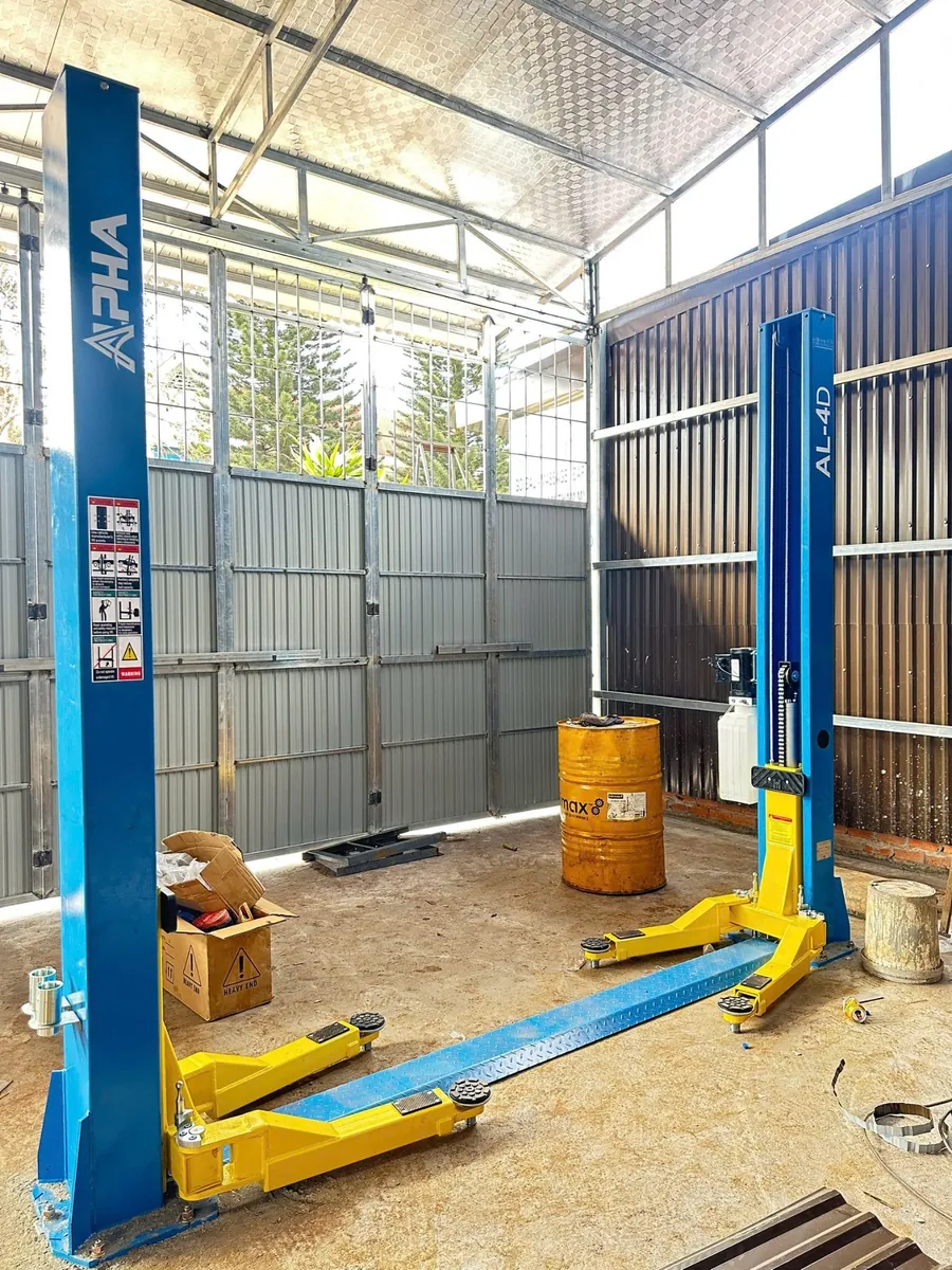 Cầu nâng ô tô 2 trụ Alpha AL-4D màu xanh vàng, đã được lắp đặt trong garage.
