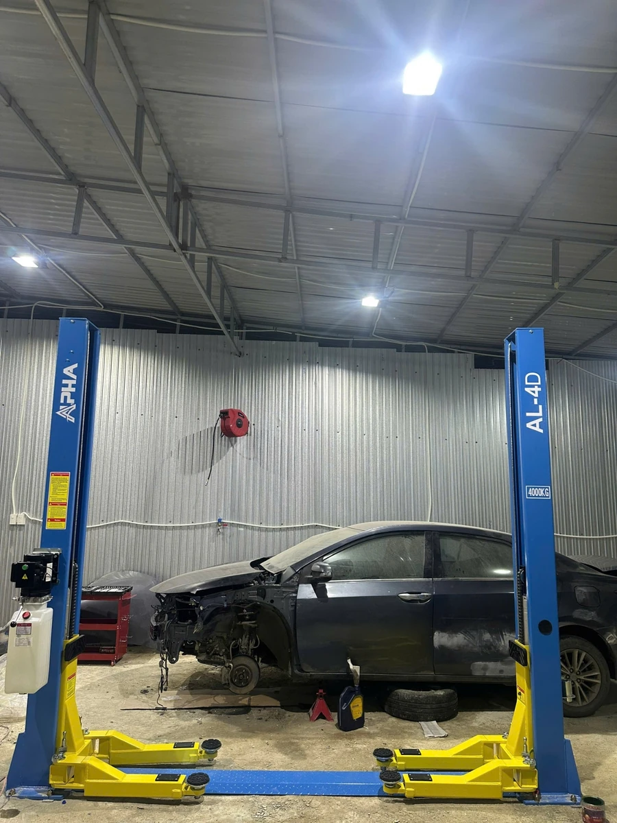 Cầu nâng ô tô 2 trụ Alpha AL-4D đang nâng một chiếc xe sedan tối màu để sửa chữa.