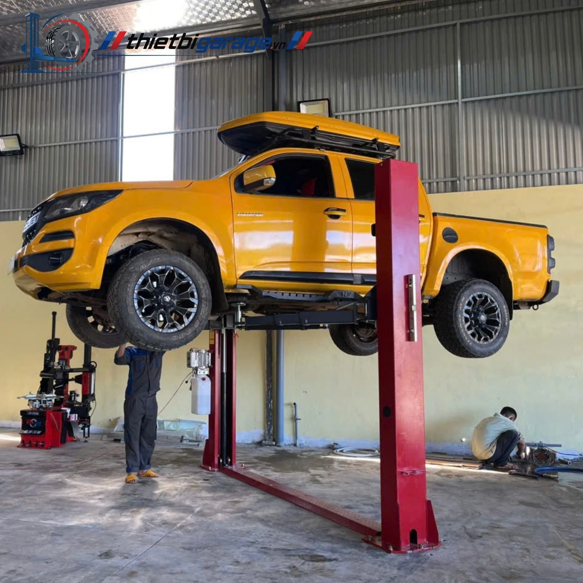 Cầu nâng ô tô 2 trụ Suntek 4000D đang nâng một chiếc xe bán tải màu vàng.