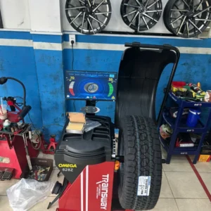 Máy cân bằng lốp OMEGA TRAINSWAY 828Z chính hãng đang hoạt động tại garage, màn hình hiển thị thông số kỹ thuật.